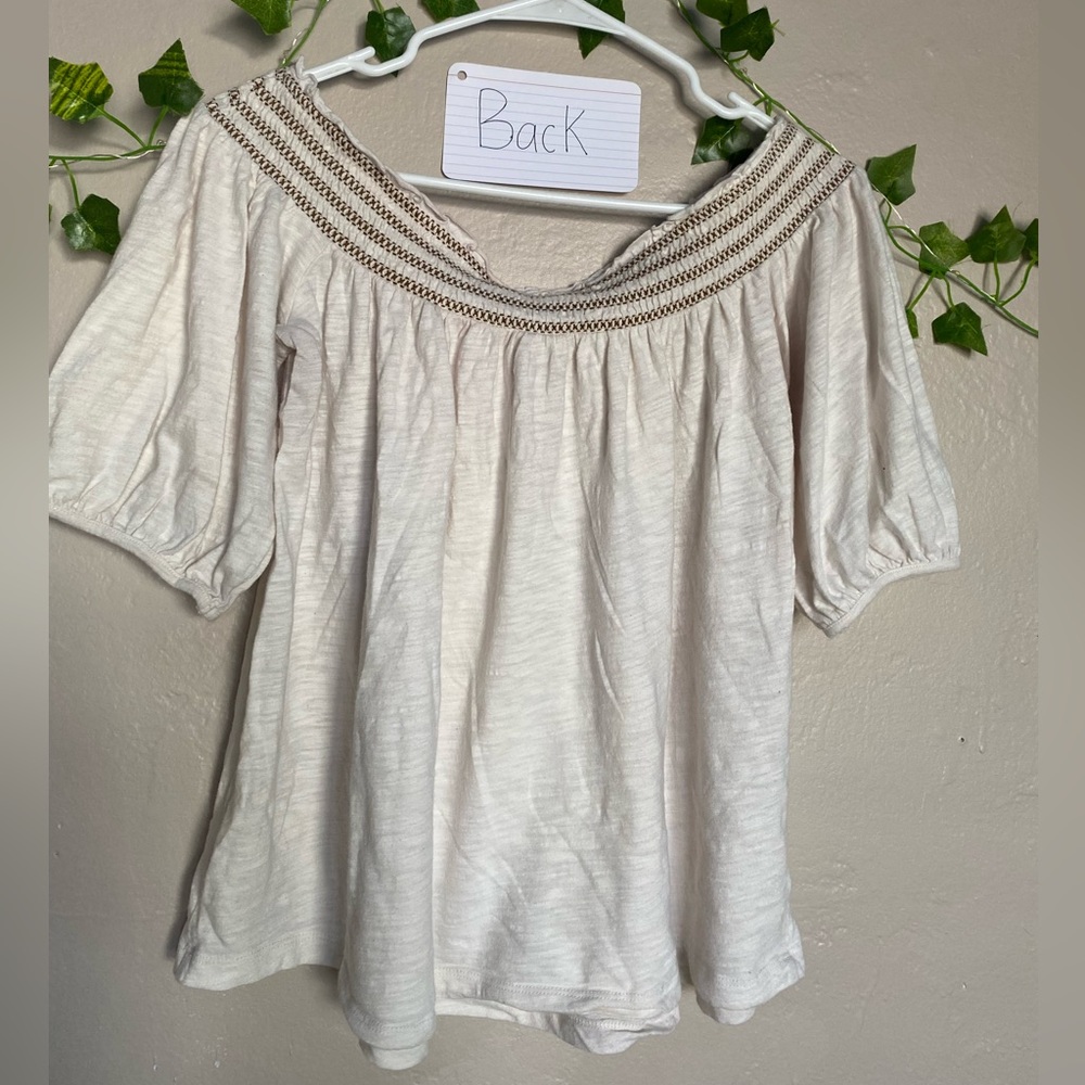 Cream color over-the-shoulder blouse with brown stitching around the top.